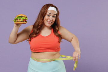 Young smiling chubby overweight plus size big fat fit woman in red top warm up training hold fast food burger put measuring tape on waist isolated on purple background home gym. Workout sport concept - Powered by Adobe