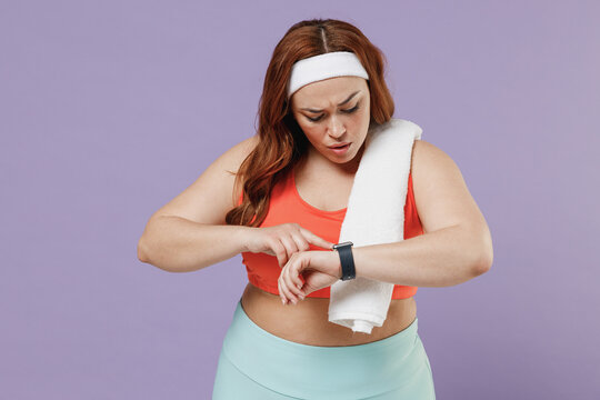 Young chubby overweight plus size big fat fit woman in red top towel warm up training look at smart watch using app settings isolated on purple background home gym Workout sport motivation concept