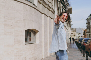 Fototapeta premium Side profile view young tourist excited caucasian woman 20s in jeans clothes eyeglasses walk in city center street near building point index finger aside. People urban youth travel lifestyle concept