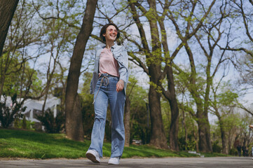 Full length bottom view young smiling fun confident woman 20s wearing trendy jeans clothes walking...