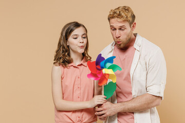 Young joyful parent man have fun with child teen girl in casual clothes Daddy little kid daughter blowing on toy windmill isolated on beige background studio portrait Father's Day Love family concept