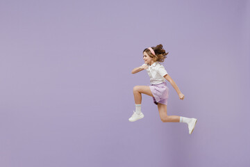 Full length side view of little fun overjoyed kid girl 12-13 years old in white short sleeve shirt jumping high run fast hurrying up isolated on purple background Childhood children lifestyle concept