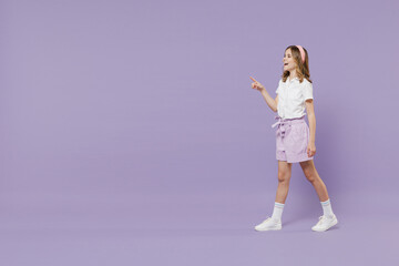 Full length fun little kid girl 12-13 years old in white shirt walk point index finger aside on copy space advert promo area isolated on purple color background. Childhood children lifestyle concept.