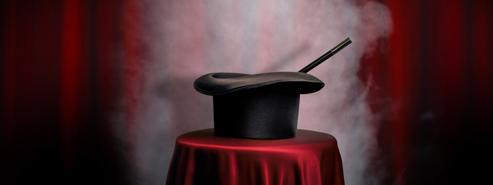 Magician top hat, wand and magician table on a theatre stage with red curtains