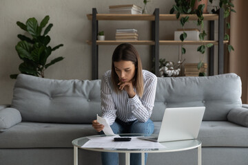 Concentrated thoughtful young woman holding paper bills, involved in financial paperwork or...