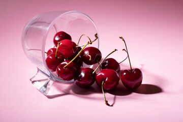 glass container lying on a pink background with cherries coming out of it