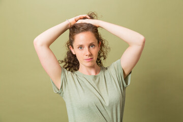 Fototapeta premium portrait pretty redhead smiling girl with hands in hair looking at camera with green t-shirt on green background