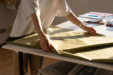 Closeup of unrecognizable female sewer holding cloth for cutting while work in workshop studio. Creative process in atelier concept. Woman tailor create clothes design with trendy fabric material