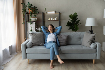 Happy young beautiful barefoot woman relaxing on comfortable sofa, daydreaming or visualizing...