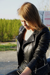 The girl, blonde in a leather jacket, smiles at the sun and is embarrassed, with blonde hair.