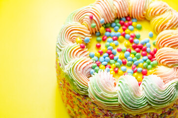 Madeira sponge coated with yellow colour frosting, layered with plum and raspberry jam, filled and topped with multicolour chocolate nibs and decorated with multicolour frostings and sugar decorations