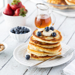 A stack of buttermilk pancakes topped with blueberries and banana, ready for syrup to be poured on...