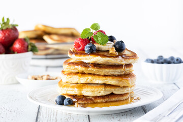 Close up of a stack of buttermilk pancakes topped with berries, banana and syrup and garnished with...