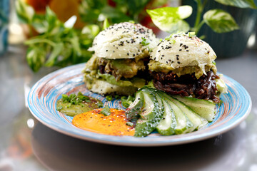 Sandwich with vegetables, fried red onion and avocado salad served with fresh cucumber and humus.
Dish on a plate, food photography, serving proposal.