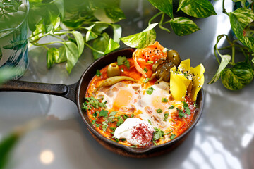 Shakshouka, fried eggs in a pan with vegetables and tomatoes.
Breakfast, eggs with vegetables served in a pan.