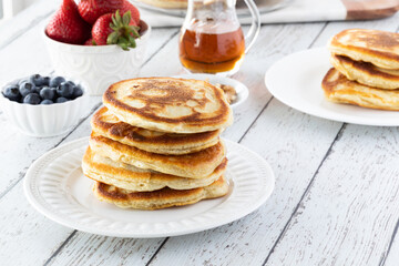 A fresh stack of warm buttermilk pancakes ready for toppings, on a light wooden table.