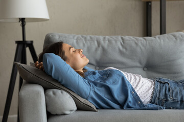 Side view smiling peaceful mindful young woman lying on comfortable sofa, meditating or visualizing...