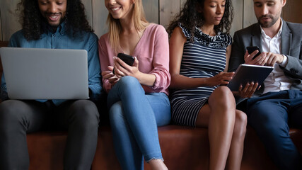 Cropped image young friendly multiracial people sitting on comfortable couch, involved in using different devices. Happy mixed race friends sharing applications or funny information, tech addiction. - Powered by Adobe
