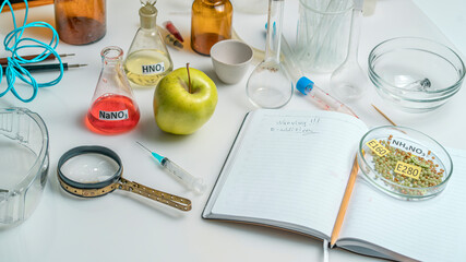 Food safety laboratory. View of a fresh ripe apple with test tubes and tools on a table with an open notepad in a research laboratory. The concept of genetic modification of fruits.