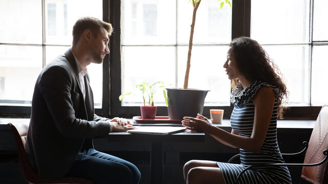 Concentrated young male financial advisor, travel agent or realtor listening to african american female client, consulting at meeting in cafe. Mixed race woman passing job interview with hr manager.