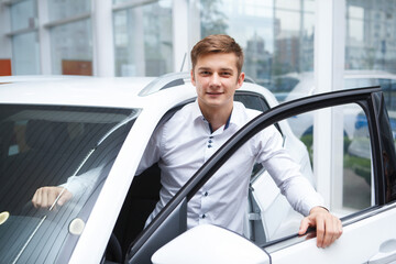 Handsome young man getting out of the new car at cauto dealership