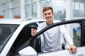 Cheerful handsome man showing car key, celebrating buying new auto at the dealership