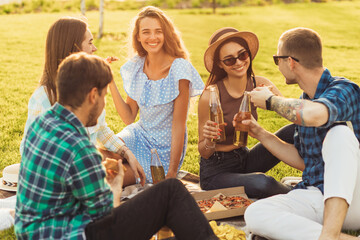 young students having a picnic in the park on the grass, Young friends enjoying warm sunny days eating pizza and drinking drinks outdoors
