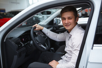 Young man choosing new car to buy at dealership salon, sitting in a new auto