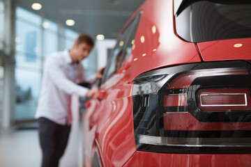 Selective focus on car lights, male customer examining auto at the dealership on background