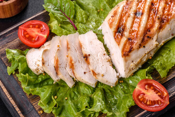 Pieces of chicken, tomatoes and lettuce leaves on a dark concrete background