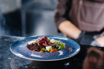 A professional chef serves a freshly prepared salad of tomato and veal greens with sauce in a gourmet restaurant close-up.