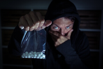 Drogendealer mit Drogen Pillen in d&uuml;sterer Umgebung in schwarzer Kapuze