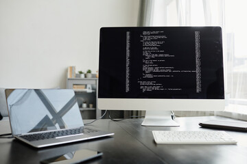 Close-up of computer monitor with software uploading on it and laptop on the workplace in office