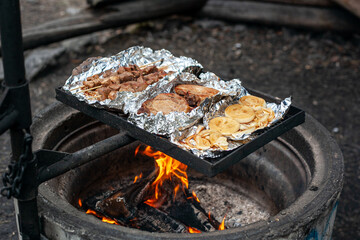 Pork kebab, pork steaks and onions are grilled on the foil over a campfire.