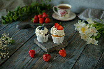 two cupcakes decorated with strawberries and blueberries on a wooden background, homemade cakes, fruits, breakfast



