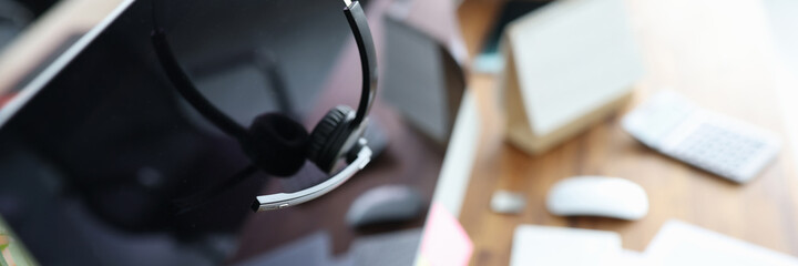 Obraz na płótnie Canvas Headphones with microphone hanging on computer monitor closeup