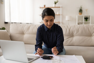 Young Indian woman manage family budget calculate finances pay bills taxes online. Millennial mixed race female count consider expenses expenditures, make payment on computer. Banking concept.