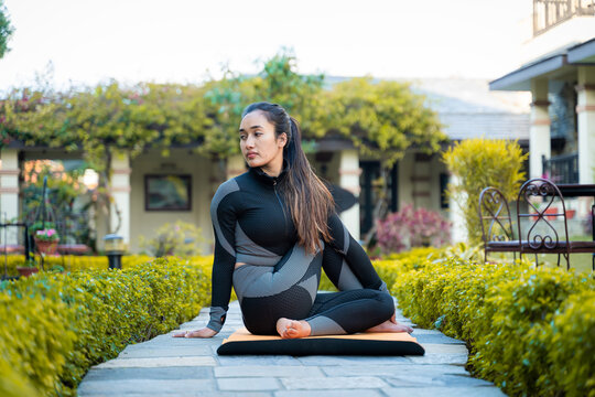 Beautiful yogi girl in black sports wear practicing yoga, sporty young girl sitting in matsyendrasana pose, exercising in garden.
