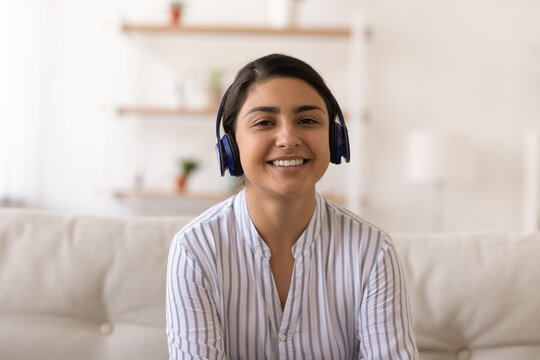 Screen view portrait of smiling millennial Indian woman in earphones sit on sofa have webcam online digital communication. Happy young mixed race in headphones talk speak on video call at home.