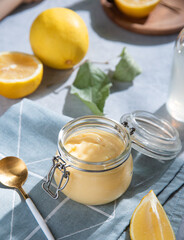 homemade lemon curd  in a glass jar with lemon slices  on a blue background. Concept breakfast with morning shadows