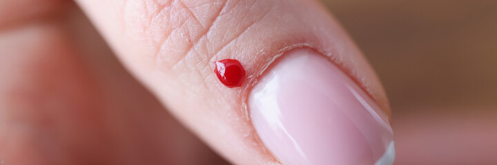 Closeup of drop of blood near womans nail