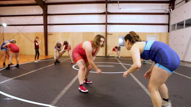Pair of female wrestlers drilling takedowns during a coed group wrestling practice.