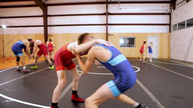 Pair of teenage wrestlers drilling takedowns during a coed group wrestling practice.