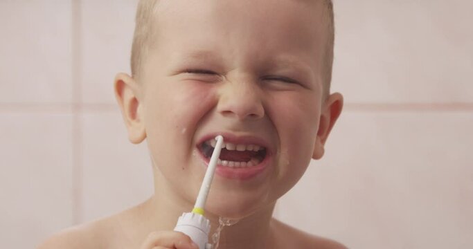 Close-up of Little Boy Holding Water Flosser and Cleaning His Teeth while Looking at Camera in a Bathroom

