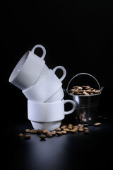 White coffee cups and roasted coffee in a bucket on a dark background in the studio. Coffee concept