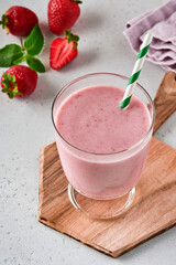 Strawberry smoothie or milkshake with berries and mint in tall glass on light grey background. Summer drink shake, milkshake and refreshment organic concept. Place for text.