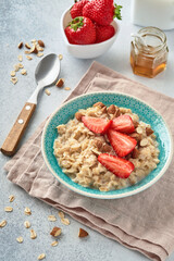 Oatmeal porridge with strawberry slices, nuts almonds and honey in blue bowl on grey table. Healthy eating, dieting, vegetarian food concept. Place for text