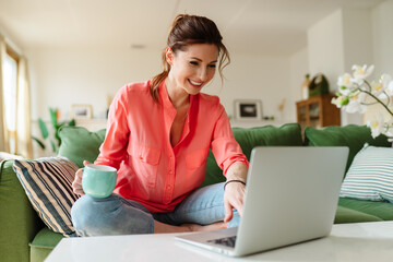 Portrait of a woman sitting on the couch at home, communicating via video link with relatives....