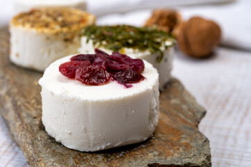 Cheese collection, variety of fresh white soft goat French cheeses with aromatic herbs, berries and green pesto