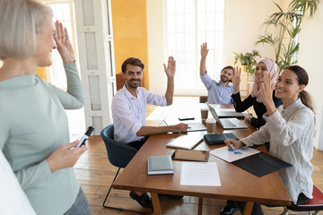 Successful smiling diverse employees team with middle aged business coach mentor raising hands,...
